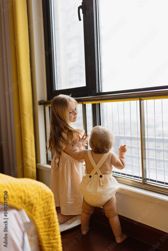 Little sister and her baby brother. Toddler kid playing with new sibling. Girl and baby 1 year old relax in a home bedroom. Family with two children at home. Love, trust and tenderness concept Little sister and her baby brother. Toddler kid playing with new sibling. Girl and baby 1 year old relax in a home bedroom. Family with two children at home. Love, trust and tenderness concept