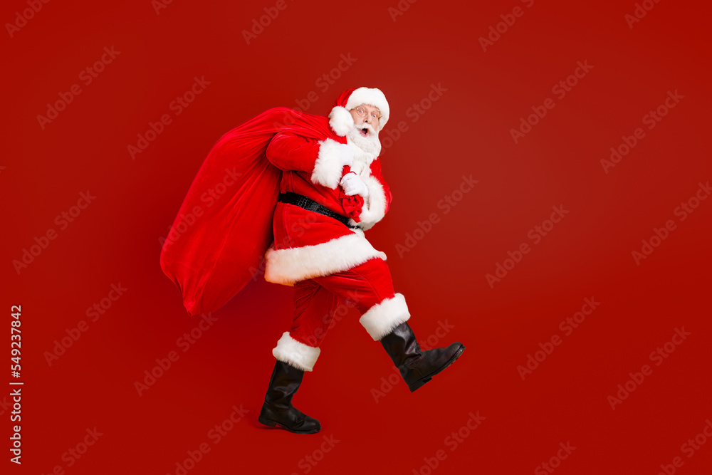 Full length body size profile side view of his he nice funny cheery amazed white-haired Santa carrying big large sack custom tradition isolated bright vivid shine vibrant yellow color background Full length body size profile side view of his he nice funny cheery amazed white-haired Santa carrying big large sack custom tradition isolated bright vivid shine vibrant yellow color background