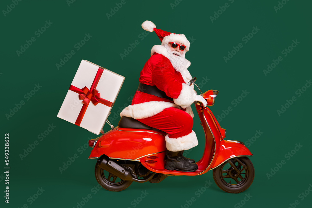 Full length profile side photo of grey white hair bearded santa claus ride drive bike deliver gift box x-mas christmas night wear red headwear isolated yellow color background Full length profile side photo of grey white hair bearded santa claus ride drive bike deliver gift box x-mas christmas night wear red headwear isolated yellow color background