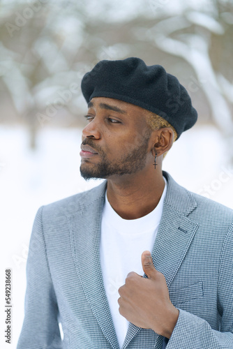 Young man in beret like Che Guevara stay on winter background. African american hold jacket looking aside.