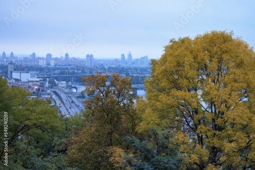 Aerial autumn landscape view of Kyiv. Yellow leaves tree. Ancient Podil neighborhood and river Dnipro with several bridges at the background. Autumn foggy morning. Travel and tourism concept