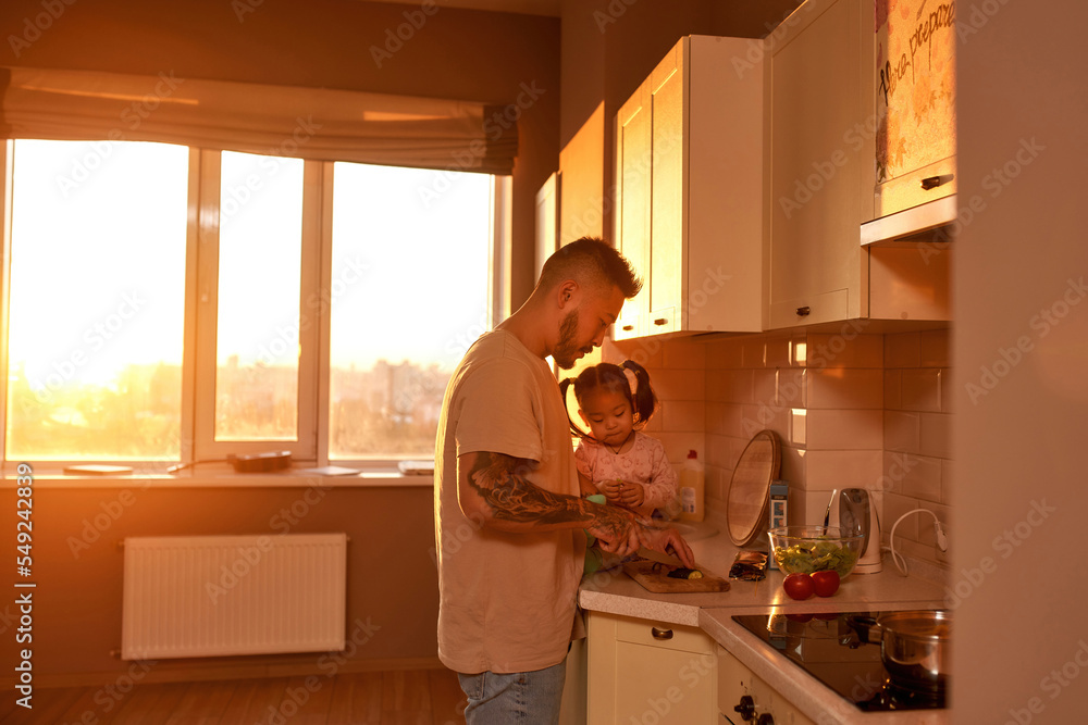 Man cut cucumber near little daughter on kitchen Man cut cucumber near little daughter on kitchen