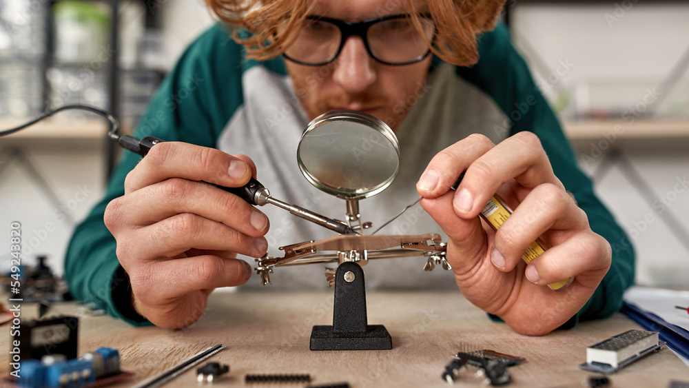 Male engineer solder chip under magnifying glass