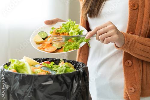 Compost from leftover food, asian young housekeeper woman hand holding cutting board use fork scraping waste, rotten vegetable throwing away into garbage, trash or bin. Environmentally responsible. photo