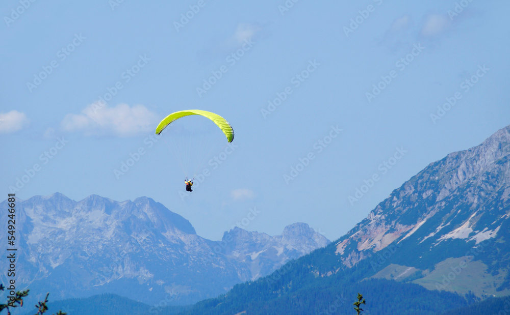 a paraglider flying over the vast alpine valley surrounded by the Austrian Alps of the Schladming-Dachstein region on a sunny summer day (Schladming, Austria)