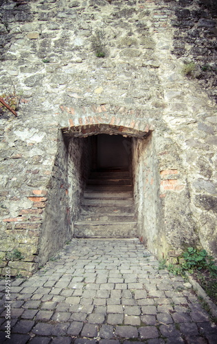 Fototapeta Naklejka Na Ścianę i Meble -  Passage between two parts of the ancient castle with an old stone staircase. Stone arch and steps in the castle. Stone corridor with stairway in ancient castle. Secret entrance