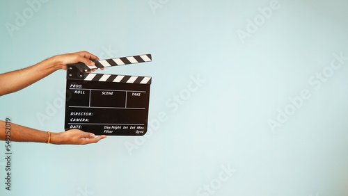 Slika na platnu Hand is holding clapper board or clapperboard or movie slate, used in film production and cinema ,movies industry isolated over blue background