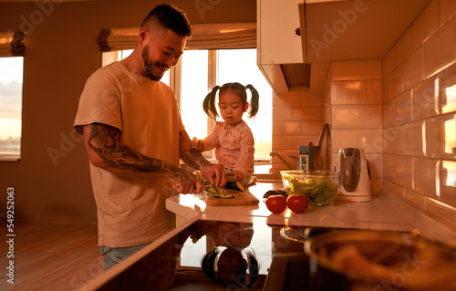 Asian girl look at father cut cucumber for salad