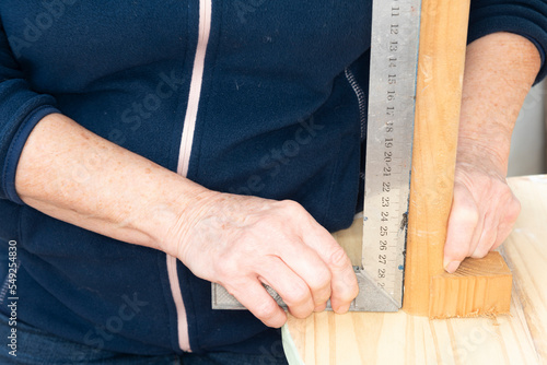 Carpintero colocando una pata de la mesa de madera recta, con la ayuda de una escuadra de metal photo