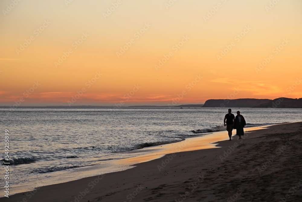 Silhouette of a couple walking at the beach at sunset. 