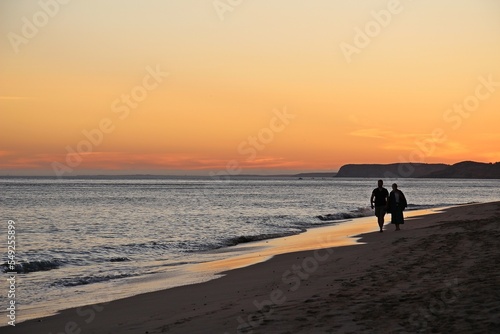 Silhouette of a couple walking at the beach at sunset. 