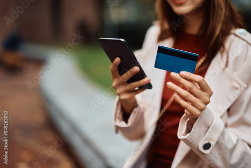 Close up of woman using credit card and mobile phone outdoors.