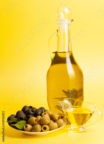 Jug with olive oil, green and black olives on yellow background.