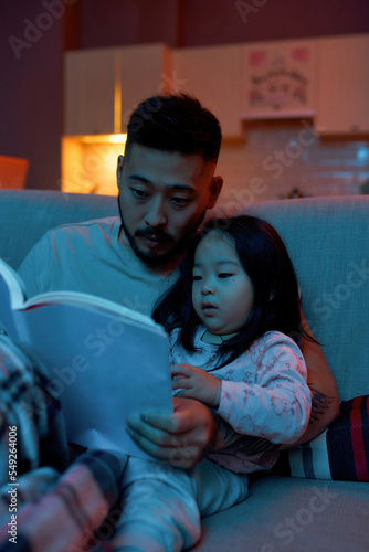 Father reading book to little daughter on sofa