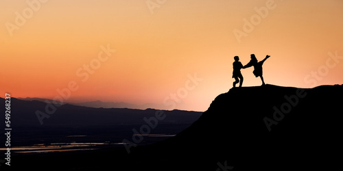 Silhouette of a dancing couple on a rock 