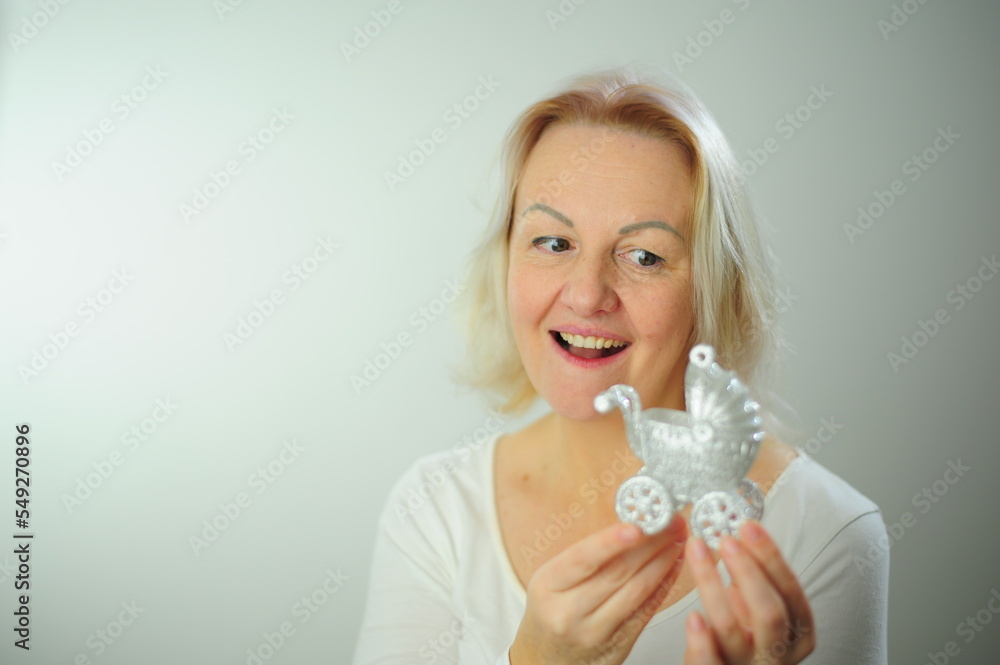 Adult beautiful woman with blond hair holds in her hands Silver baby carriage Christmas tree toy baby birth invitation Place for text party Baby's birthday Joy of happiness the emergence of a new life Adult beautiful woman with blond hair holds in her hands Silver baby carriage Christmas tree toy baby birth invitation Place for text party Baby's birthday Joy of happiness the emergence of a new life