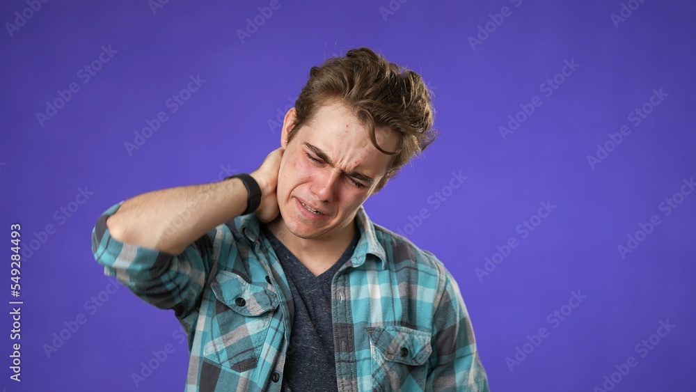 Portrait of young hipster man 20s with sore neck shoulder problem isolated on purple background in studio Portrait of young hipster man 20s with sore neck shoulder problem isolated on purple background in studio
