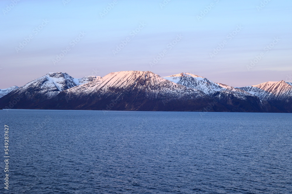 Sonnenaufgang an der Küste bei Alta in Norwegen. Die Berge werden von der Sonne angestrahlt.