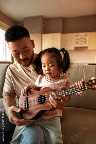 Father teach daughter play notes on ukulele