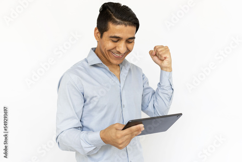 Successful man with tablet. Indian man in blue shirt celebrating victory with clenched fist. Portrait, studio shot, technology, success concept