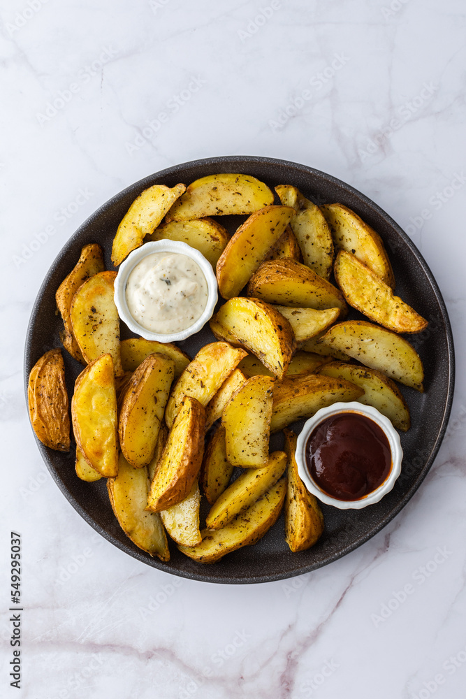Oven roasted potatoes with skins, sliced, with sauces close-up, top view Oven roasted potatoes with skins, sliced, with sauces close-up, top view