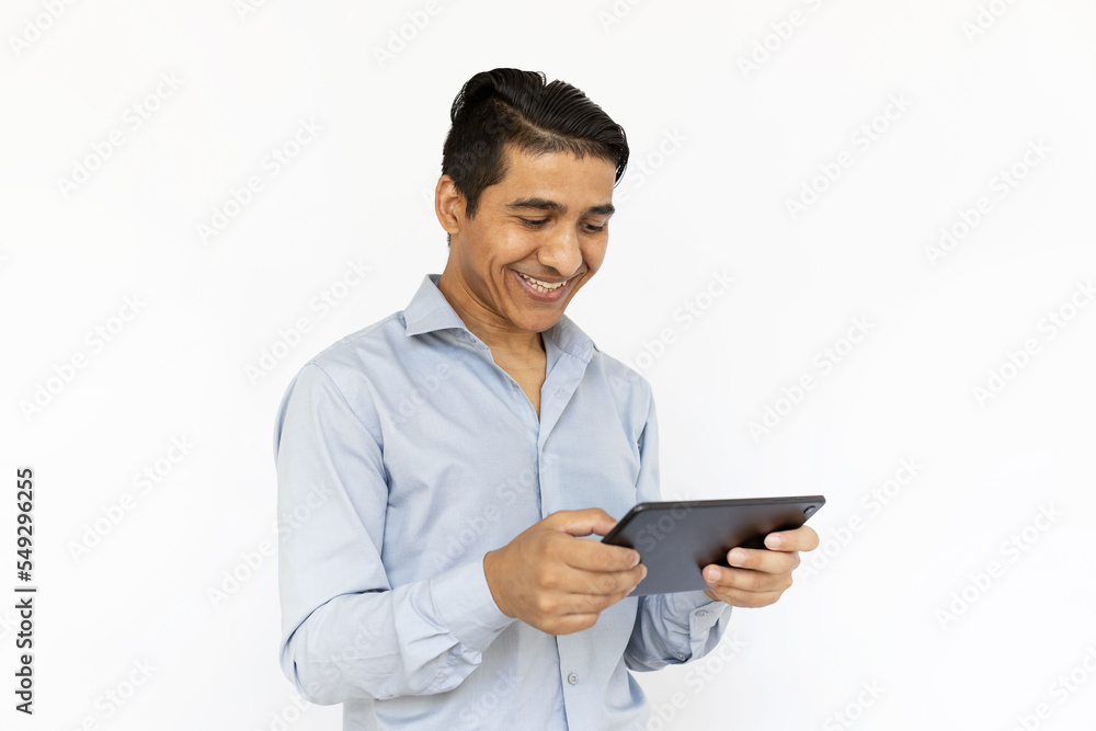 Satisfied man holding tablet with both hands. Indian man in blue shirt smiling and checking tablet. Portrait, studio shot, technology concept Satisfied man holding tablet with both hands. Indian man in blue shirt smiling and checking tablet. Portrait, studio shot, technology concept