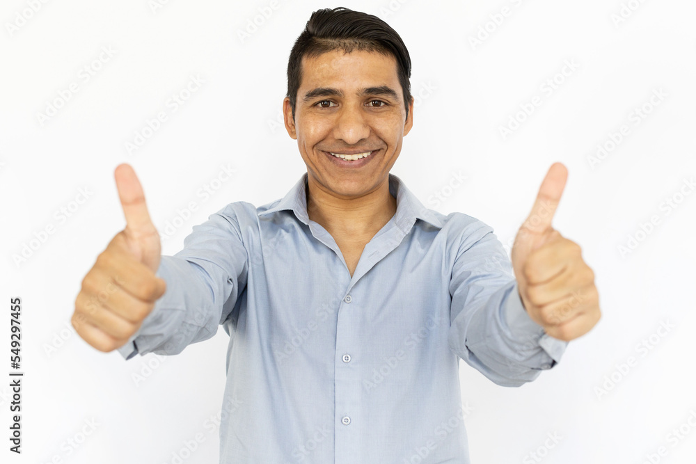 Cheerful man showing thumbs up. Indian man in blue shirt smiling, looking at camera and making like gesture. Portrait, studio shot, quality, joy concept Cheerful man showing thumbs up. Indian man in blue shirt smiling, looking at camera and making like gesture. Portrait, studio shot, quality, joy concept