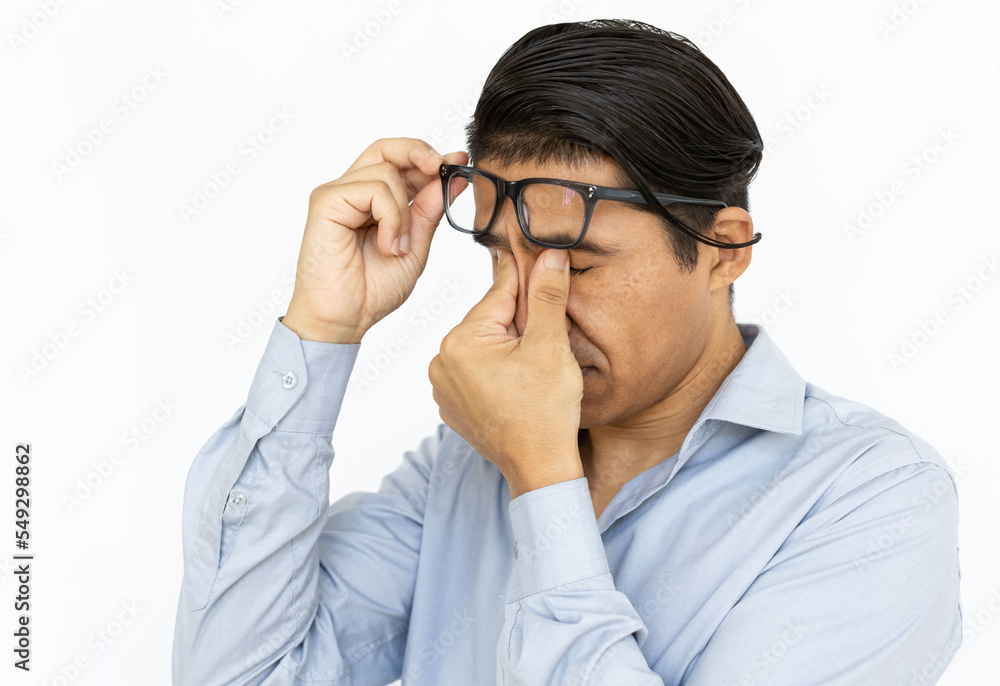 Tired man rubbing eyes. Indian man in blue shirt raising glasses, taking break. Portrait, studio shot, stress concept Tired man rubbing eyes. Indian man in blue shirt raising glasses, taking break. Portrait, studio shot, stress concept