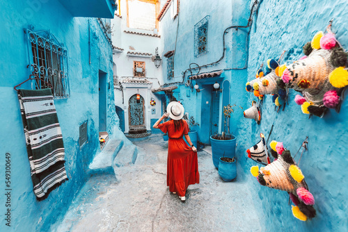 Young woman with red dress visiting the blue city Chefchaouen, Marocco - Happy tourist walking in Moroccan city street - Travel and vacation lifestyle concept © Davide Angelini