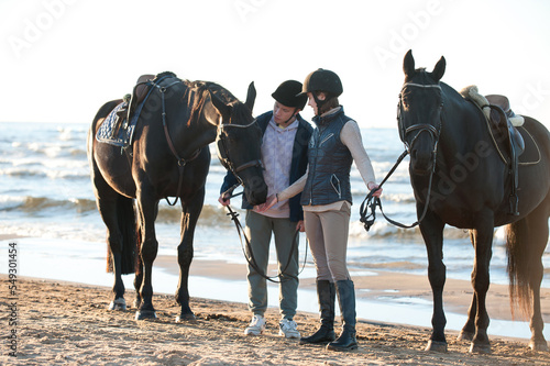 Young couple smiling standing together with horses at wavy sea