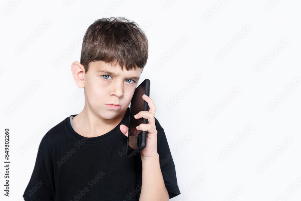 Upset young boy holding a modern phone and talking to his mom, listening to a remark from mother about his bad behavior at school Upset young boy holding a modern phone and talking to his mom, listening to a remark from mother about his bad behavior at school