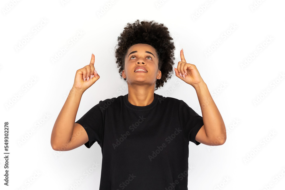 Portrait of happy young woman pointing upwards with forefingers against white background. African American woman wearing black T-shirt advertising something. Promotion concept Portrait of happy young woman pointing upwards with forefingers against white background. African American woman wearing black T-shirt advertising something. Promotion concept