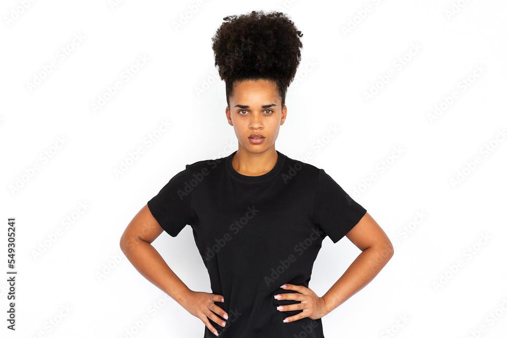 Portrait of confident young woman posing with hands on hips. African American woman wearing black T-shirt looking at camera against white background. Female beauty concept Portrait of confident young woman posing with hands on hips. African American woman wearing black T-shirt looking at camera against white background. Female beauty concept