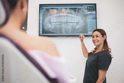 medicine, dentistry and healthcare concept - female dentist showing x-ray of teeth on tv to patient at dental clinic office.
