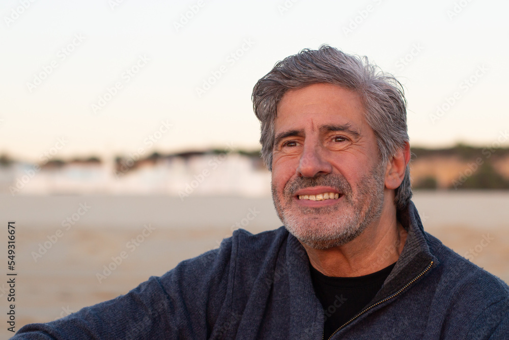 Portrait of grey-haired bearded senior man spending time outside at seashore. Smiling middle-aged man looking ahead and smiling. Medium shot. Lifestyle, retirement, leisure concept Portrait of grey-haired bearded senior man spending time outside at seashore. Smiling middle-aged man looking ahead and smiling. Medium shot. Lifestyle, retirement, leisure concept