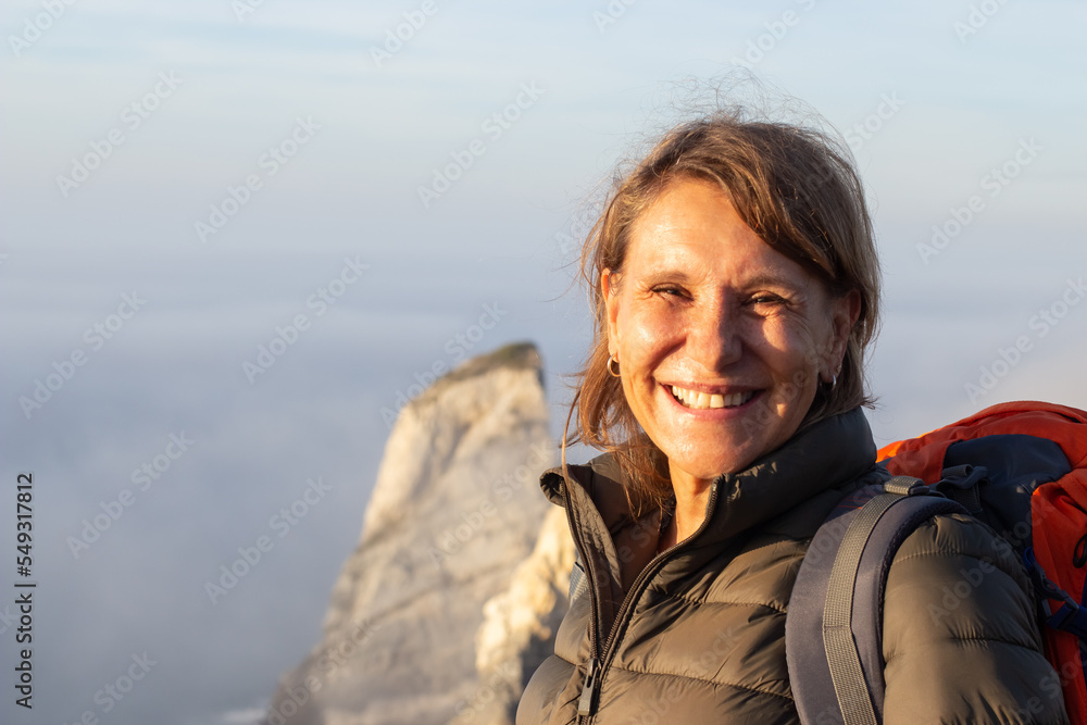Portrait of beaming elderly woman with orange backpack. Sporty woman in casual clothes looking at camera with bright smile. Sport, adventure, hobby concept