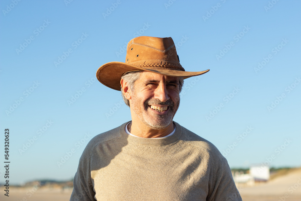 Portrait of handsome senior man in cowboy hat outside. Happy grey-haired man with beard smiling happily, enjoying sunny day. Lifestyle, retirement, leisure concept