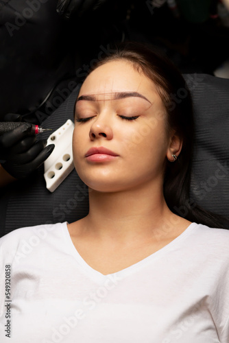 Cosmetician in gloves applying permanent powder brow makeup