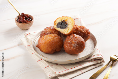 Several deep fried sweet balls made of yeast dough - donuts with poppy and cherry filling on a off-white plate on a checkered kitchen towel. unhealthy dessert photo