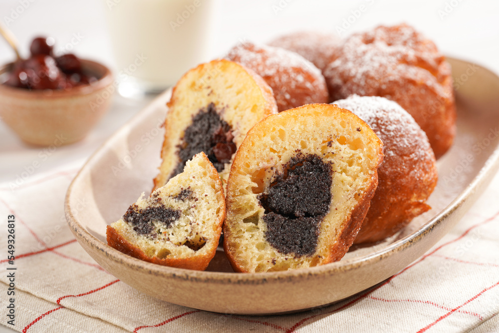 Several deep fried sweet balls made of yeast dough - donuts with poppy and cherry filling on an oval off-white plate on a checkered kitchen towel. unhealthy dessert Several deep fried sweet balls made of yeast dough - donuts with poppy and cherry filling on an oval off-white plate on a checkered kitchen towel. unhealthy dessert