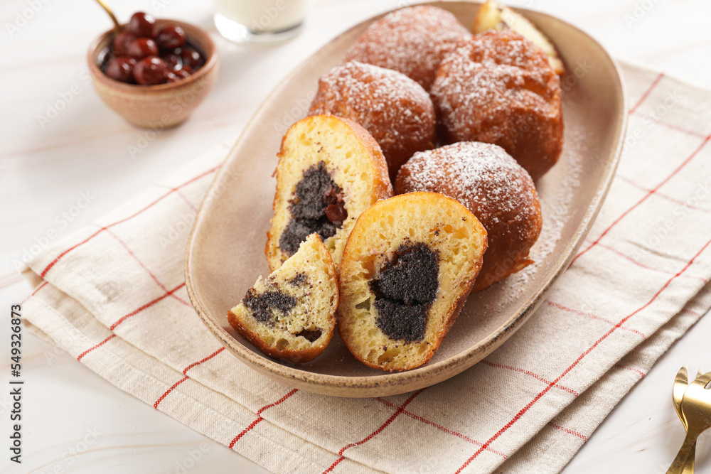 Several deep fried sweet balls made of yeast dough - donuts with poppy and cherry filling on an oval off-white plate on a checkered kitchen towel. unhealthy dessert