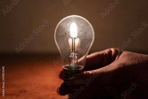 Power outage concept. Light bulb in hand by the light of a burning candle photo