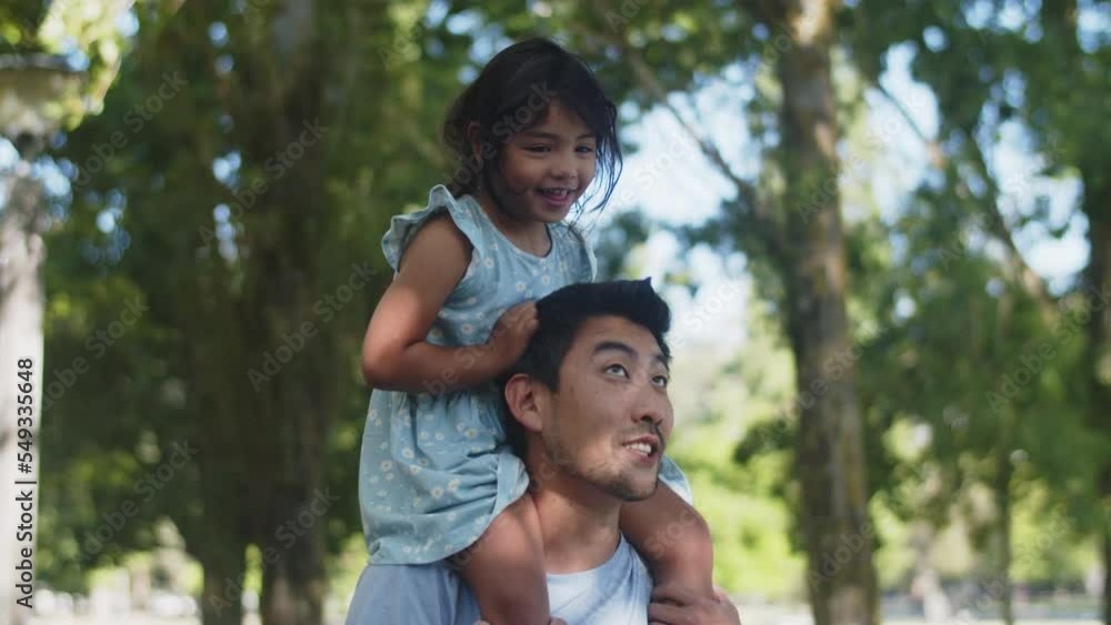 Happy Asian girl riding her father piggyback in park. Young man walking with little daughter, child laughing. Fatherhood and childhood concept Happy Asian girl riding her father piggyback in park. Young man walking with little daughter, child laughing. Fatherhood and childhood concept