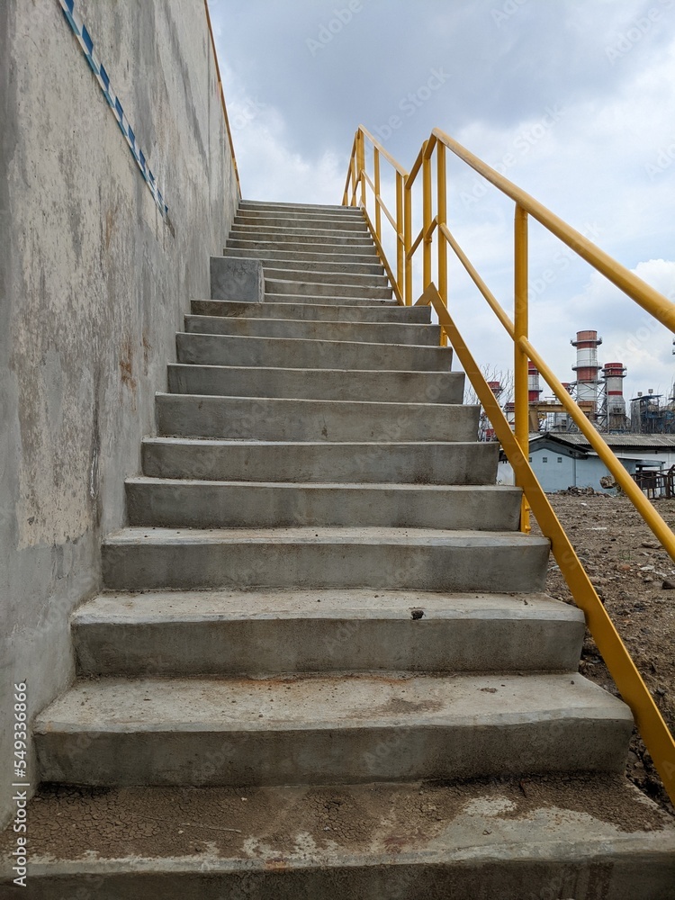 Photo concrete stair with yellow hand rail and cloudy vibes. The photo is suitable to use for industrial background and poster. Photo concrete stair with yellow hand rail and cloudy vibes. The photo is suitable to use for industrial background and poster.