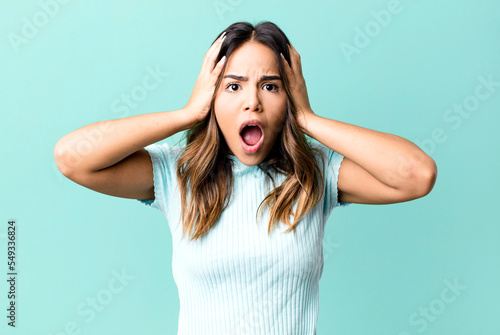 hispanic pretty woman feeling horrified and shocked, raising hands to head and panicking at a mistake