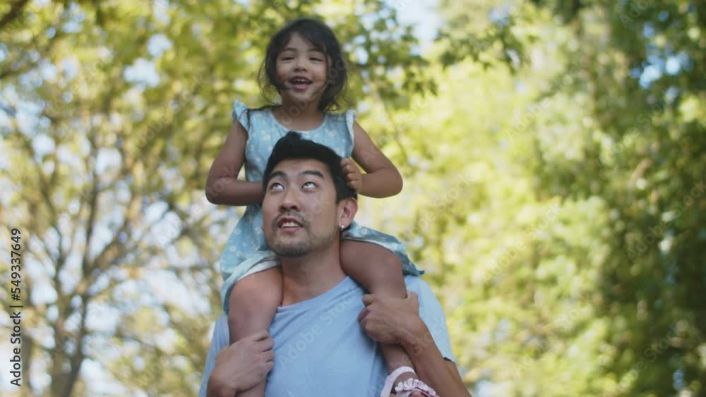 Happy young Asian man giving his daughter piggyback ride, jumping and swinging outdoors. Little girl smiling and laughing. Fatherhood and childhood concept Happy young Asian man giving his daughter piggyback ride, jumping and swinging outdoors. Little girl smiling and laughing. Fatherhood and childhood concept