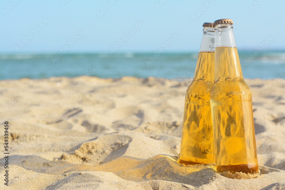 Bottles of cold beer on sandy beach near sea, space for text Bottles of cold beer on sandy beach near sea, space for text