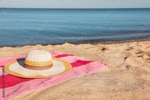 Beach towel and straw hat on sand near sea  space for text