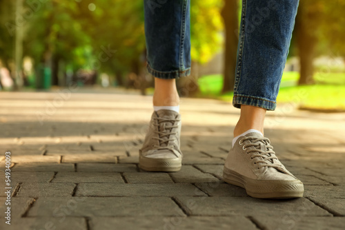 Woman in stylish sneakers walking on city street, closeup