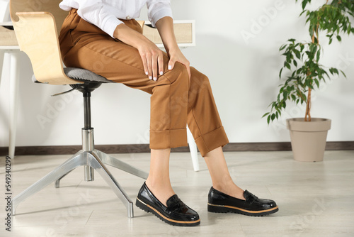 Woman rubbing sore knee in office, closeup © New Africa